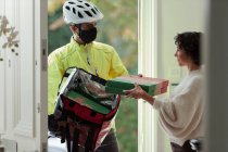 Woman receiving pizza delivery from courier in face mask at front door — Stock Photo