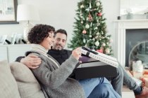 Frau öffnet Weihnachtsgeschenk ihres Mannes auf Wohnzimmersofa — Stockfoto