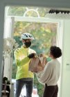 Woman receiving food delivery from courier in face mask at front door — Stock Photo