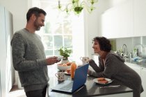 Happy couple enjoying breakfast and working at laptop in kitchen — Stock Photo