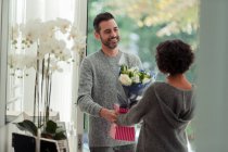 Happy husband surprising wife with flowers at front door — Stock Photo