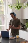 Чоловік в навушниках на відео виклик працює з дому на ноутбуці на кухні — стокове фото