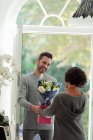 Marido feliz esposa surpreendente com flores na porta da frente — Fotografia de Stock