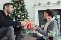 Чоловік дарує різдвяний подарунок дружині у вітальні з деревом — стокове фото