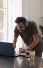 Homem com fones de ouvido trabalhando em casa no laptop na cozinha — Fotografia de Stock