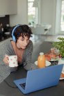 Жінка з навушниками працює з дому на ноутбуці на ранковій кухні — стокове фото