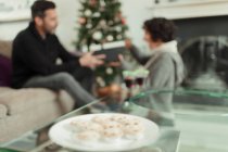 Wife opening Christmas gift from husband behind tray of mince pies — Stock Photo