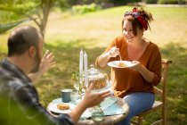 Happy couple enjoying cake and tea at sunny garden table — Stock Photo