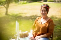 Портрет щаслива жінка насолоджується тортами за столом в сонячному літньому саду — стокове фото