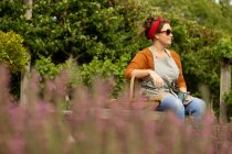Жінка в сонцезахисних окулярах відпочиває від садівництва на літньому подвір'ї — стокове фото
