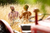 Glückliches Paar am Tisch hinter Traktor im sonnigen Sommer hohes Gras — Stockfoto