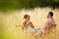 Счастливая пара отдыхает за столом в солнечной высокой траве — стоковое фото