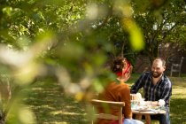 Пара насолоджується тортами за столом у сонячному літньому саду — стокове фото