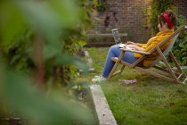 Woman working at laptop in lawn chair in summer garden — Stock Photo