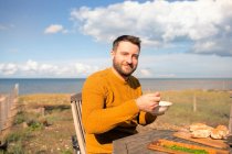 Portrait happy man eating on sunny ocean beach patio — Stock Photo
