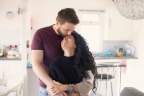 Feliz pareja cariñosa abrazándose y besándose en la cocina - foto de stock