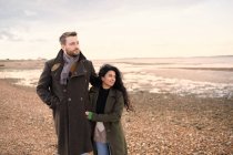 Casal afetuoso em casacos de inverno andando na praia do oceano — Fotografia de Stock