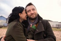 Heureux couple affectueux en manteaux d'hiver câlins sur la plage — Photo de stock