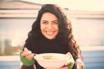 Retrato hermosa mujer feliz comer sopa en patio soleado - foto de stock