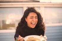 Feliz mujer riendo comiendo sopa en patio soleado - foto de stock