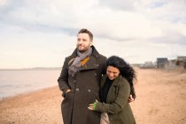Happy couple in winter coats walking on ocean beach — Stock Photo