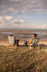 Pareja relajándose con vino en sillas de playa en el océano soleado - foto de stock
