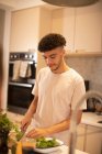 Giovane uomo che cucina tagliando verdure sul bancone della cucina — Foto stock