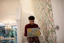 Young man using laptop on apartment stairs — Stock Photo