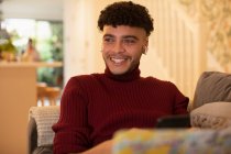 Happy young man listening to music with earbuds on sofa — Stock Photo