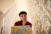 Portrait confident young man with laptop on staircase at home — Stock Photo