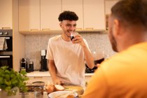 Happy gay male couple drinking wine and cooking in kitchen — Stock Photo