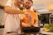 Happy gay male couple cooking in kitchen — Stock Photo