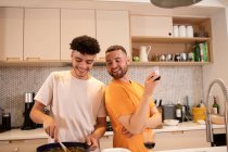 Happy gay male couple cooking and drinking wine in kitchen — Stock Photo