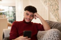 Молодой человек использует смартфон на диване в гостиной — стоковое фото
