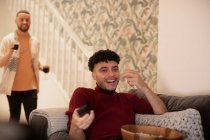Glücklicher junger Mann mit Fernbedienung vor dem Fernseher auf dem Sofa — Stockfoto
