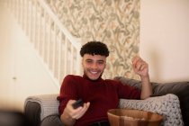 Счастливый молодой человек с пультом дистанционного управления смотрит телевизор на диване — стоковое фото