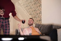 Feliz gay masculino casal aproveitando tinto vinho e assistindo TV no casa — Fotografia de Stock