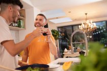 Heureux gay mâle couple boire vin et cuisine dans cuisine — Photo de stock
