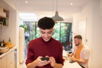 Jovem usando telefone inteligente na cozinha — Fotografia de Stock