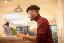 Young man working from home at laptop in kitchen — Stock Photo