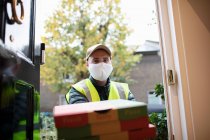 Portrait delivery man in face mask delivering pizza at front door — Stock Photo