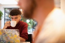 Молодой человек пьет кофе дома за ноутбуком — стоковое фото