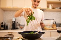 Young man cooking with fresh spinach in kitchen — Stock Photo