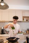 Jovem sorridente cozinhar com manjericão fresco na cozinha — Fotografia de Stock