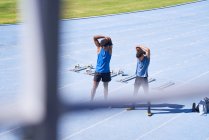Coureurs masculins étirant sur piste de sport bleu ensoleillé — Photo de stock