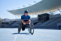 Athlète masculin en fauteuil roulant sur piste de sport bleu ensoleillé — Photo de stock