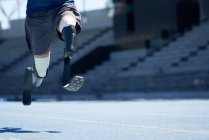 Atleta amputato di sesso maschile che corre su una pista sportiva azzurra soleggiata — Foto stock