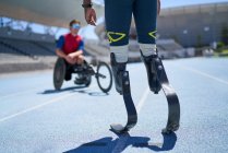 Amputado masculino e atletas de cadeira de rodas na pista de esportes azul ensolarado — Fotografia de Stock