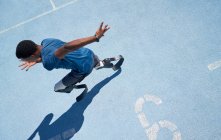 Atleta amputato di sesso maschile che corre su una pista sportiva soleggiata blu — Foto stock