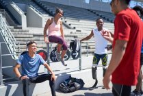 Jóvenes amigos deportistas hablando en el soleado estadio deportivo - foto de stock